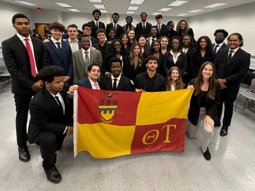 Theta Tau class photo with members in dark suits holding the fraternity flag